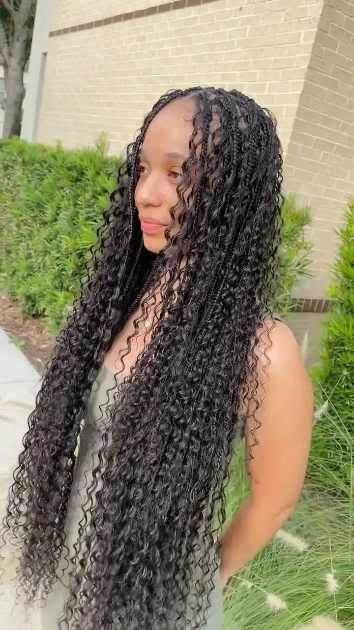Woman with long, curly hair standing outdoors near a building and greenery