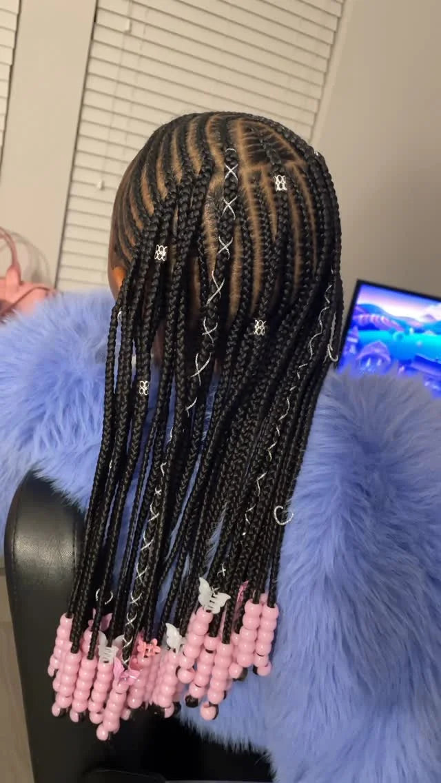 Person with braided hair extensions featuring pink beads, sitting on a blue chair.