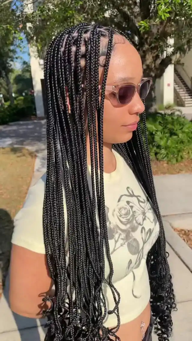 Woman with braided hair wearing sunglasses and a white t-shirt with a floral design.