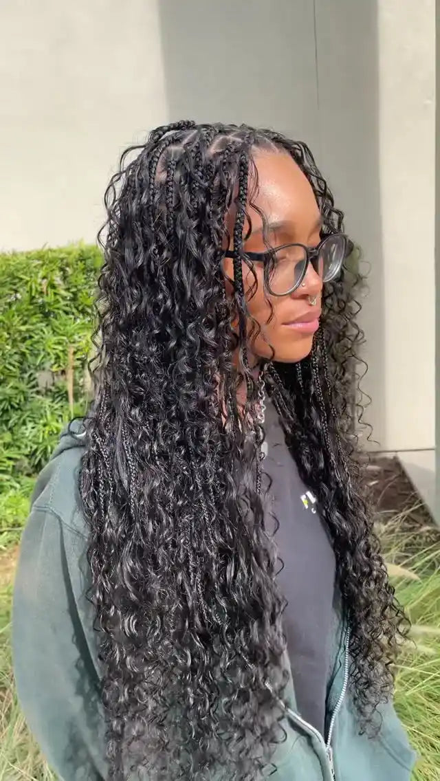 Person with long, curly hair wearing glasses outdoors.