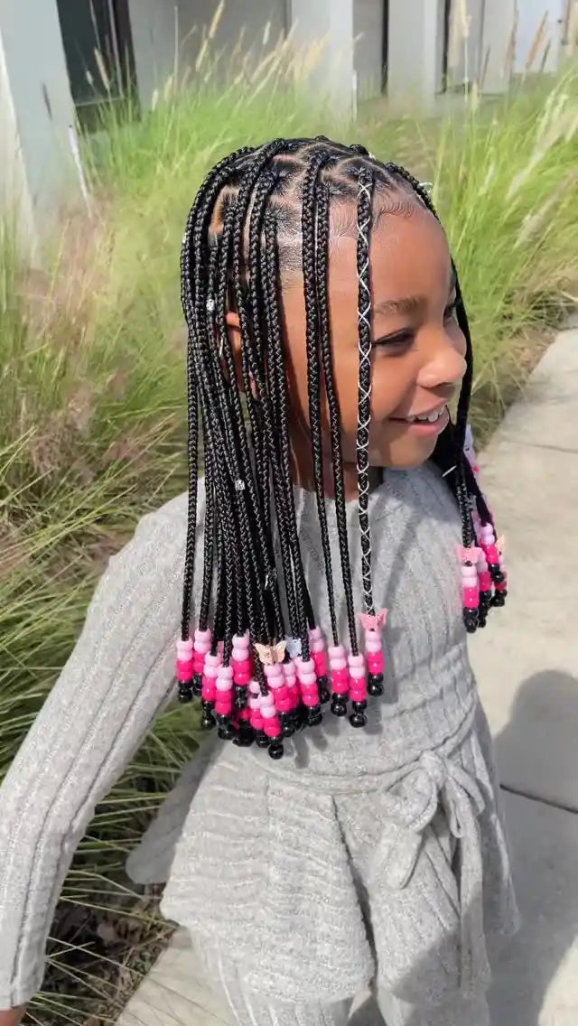 Child with braided hair featuring pink beads standing outdoors.