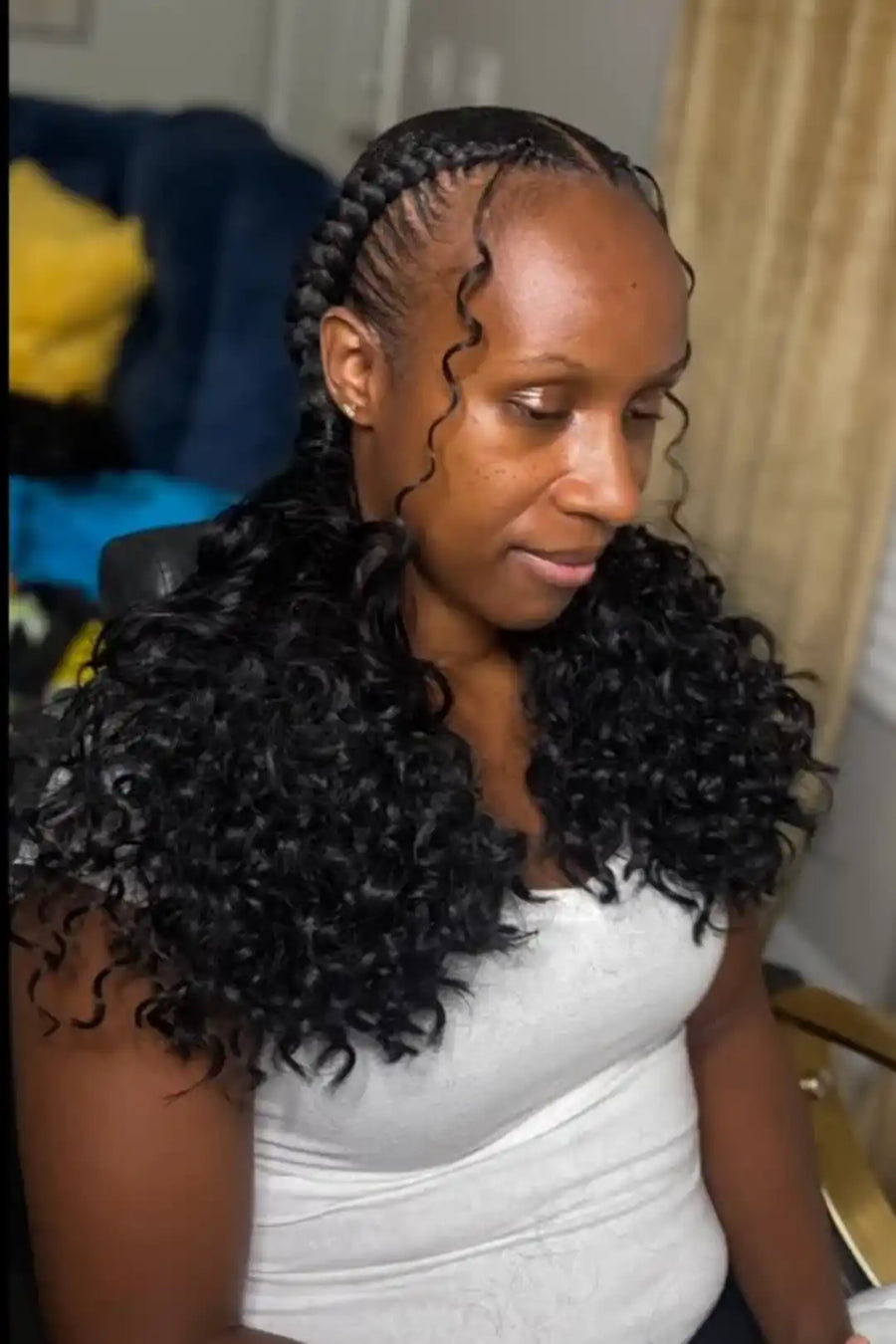 Woman with styled hair sitting indoors, wearing a white top.