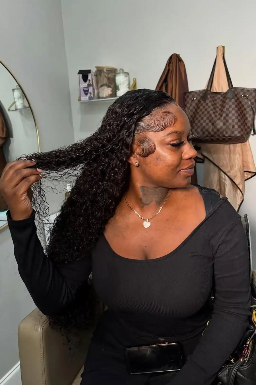 Woman adjusting a black lace wig in a room with clothing in the background