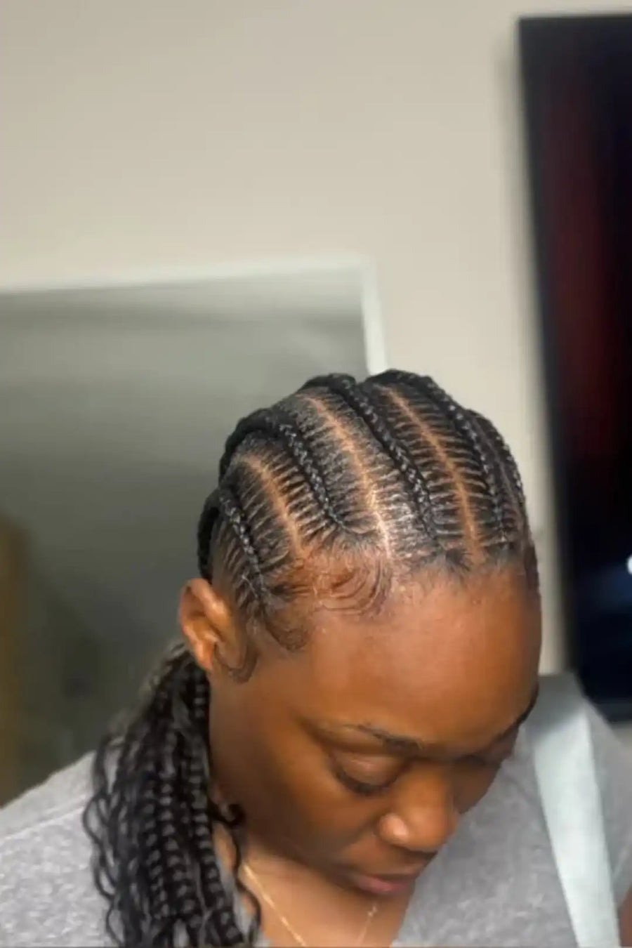 Person with braided hair wearing a gray shirt in a neutral setting