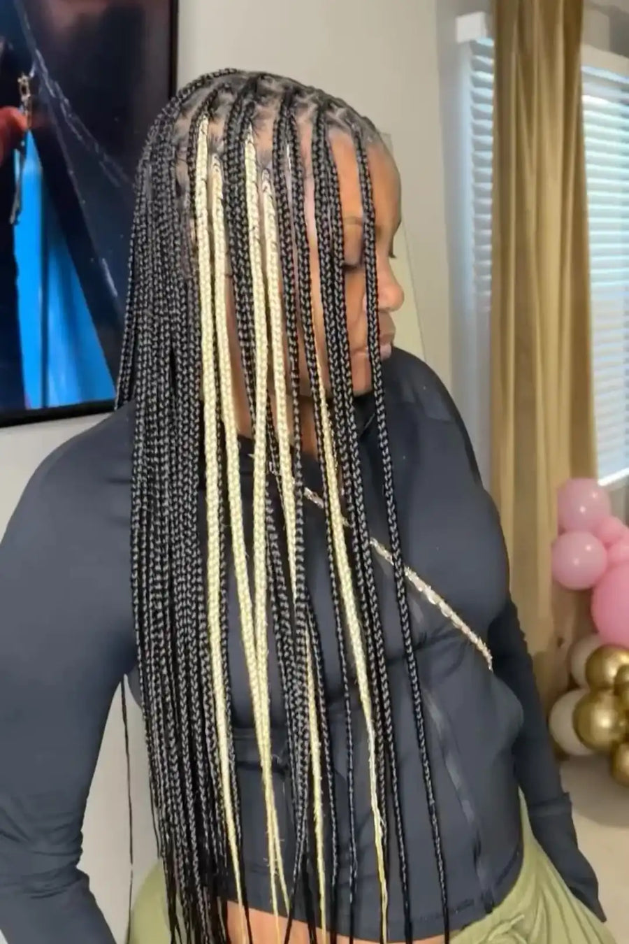 Person with braided hair in a room with balloons and a television.