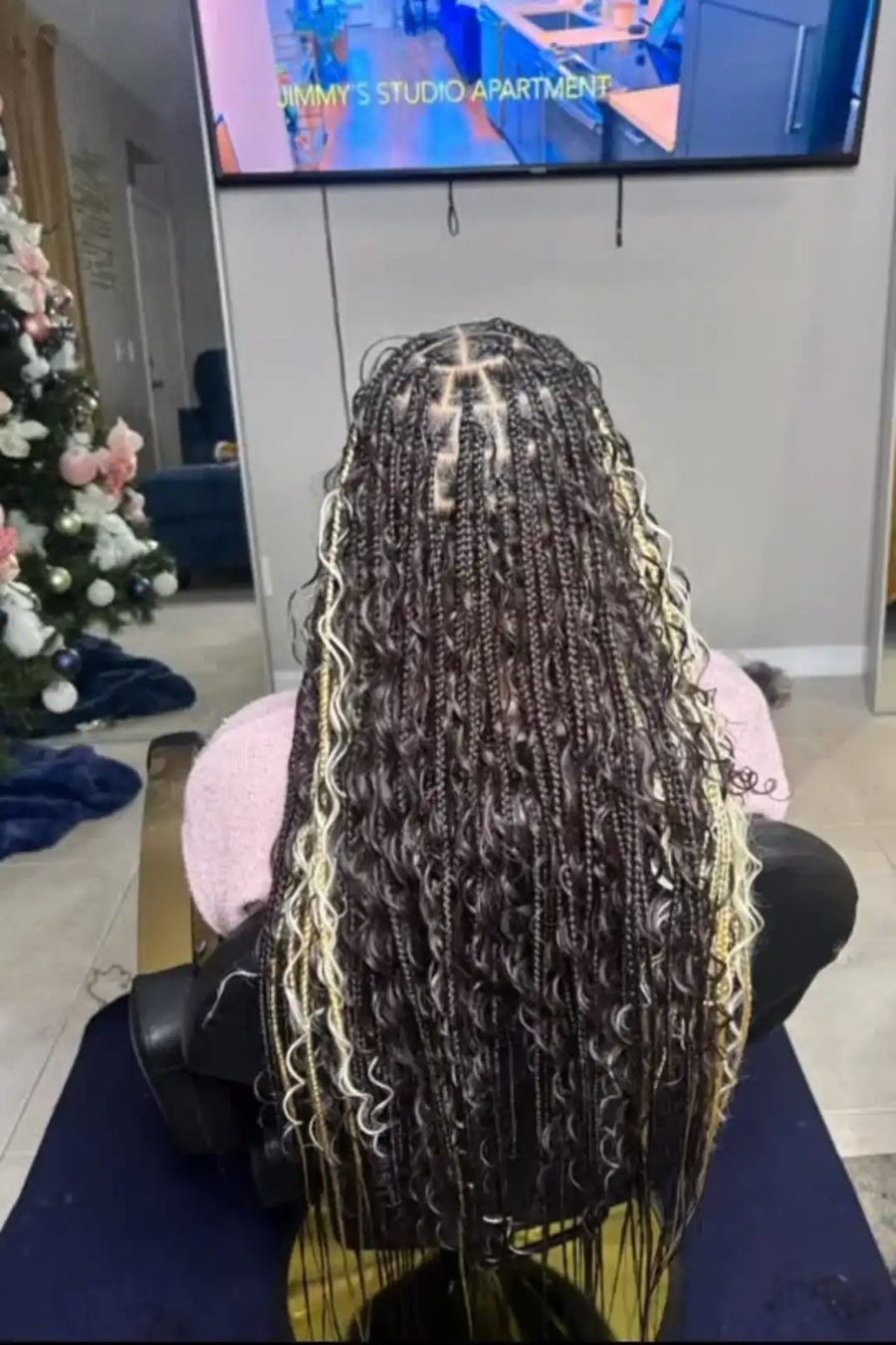 Person with braided hair sitting in a salon chair, Christmas tree and TV in the background