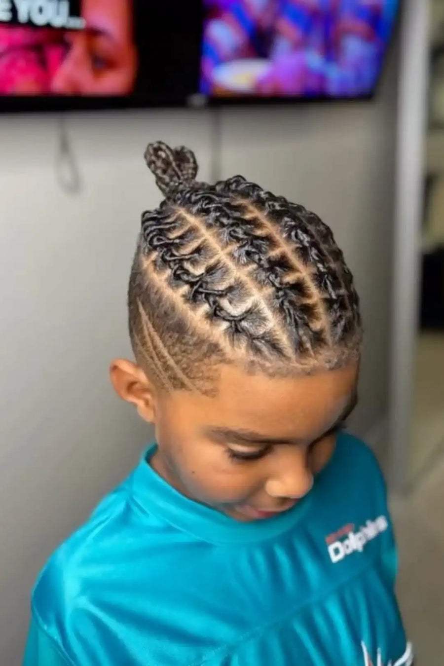Child with braided hair wearing a blue shirt with a logo