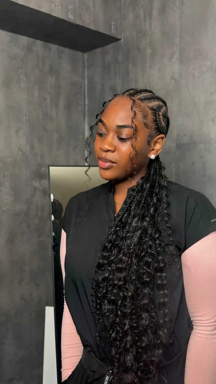 Woman with braided hair standing in front of a mirror in a bathroom.