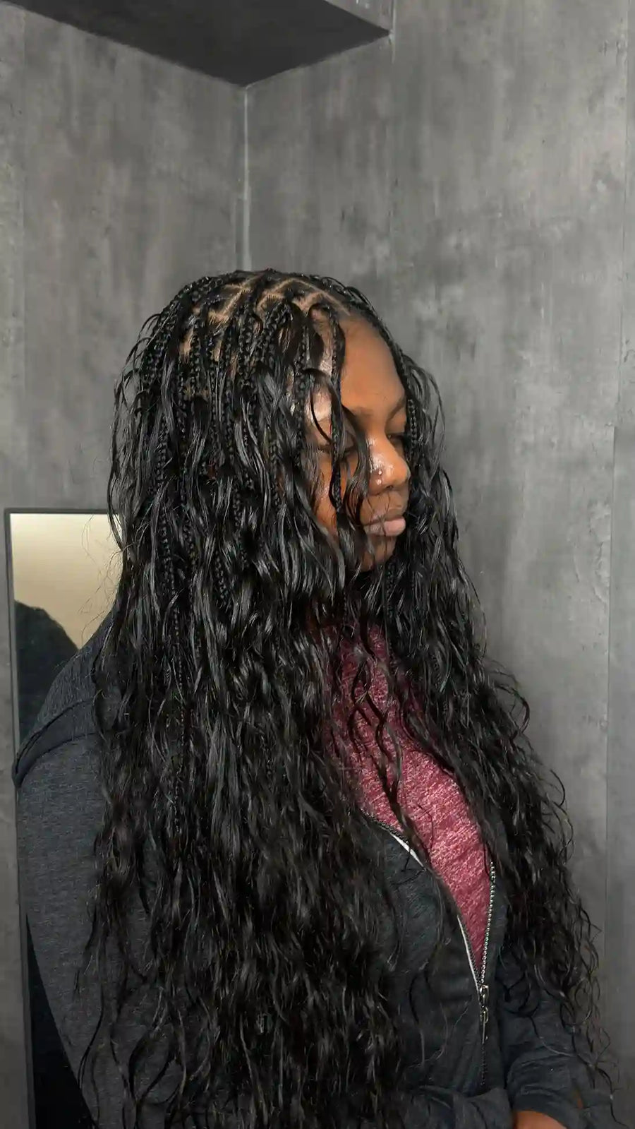 Person with long braided hair standing against a gray wall.