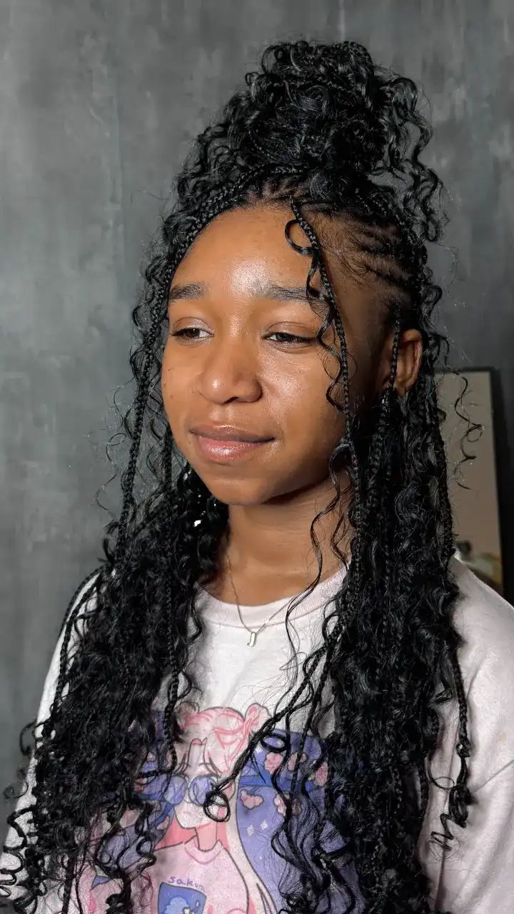 Person with braided hair wearing a colorful top against a gray background
