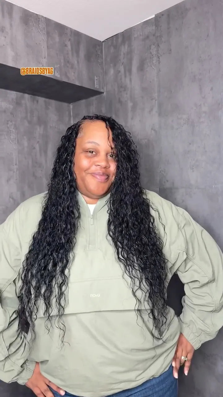 Person with long, curly hair wearing a green jacket in a gray room.