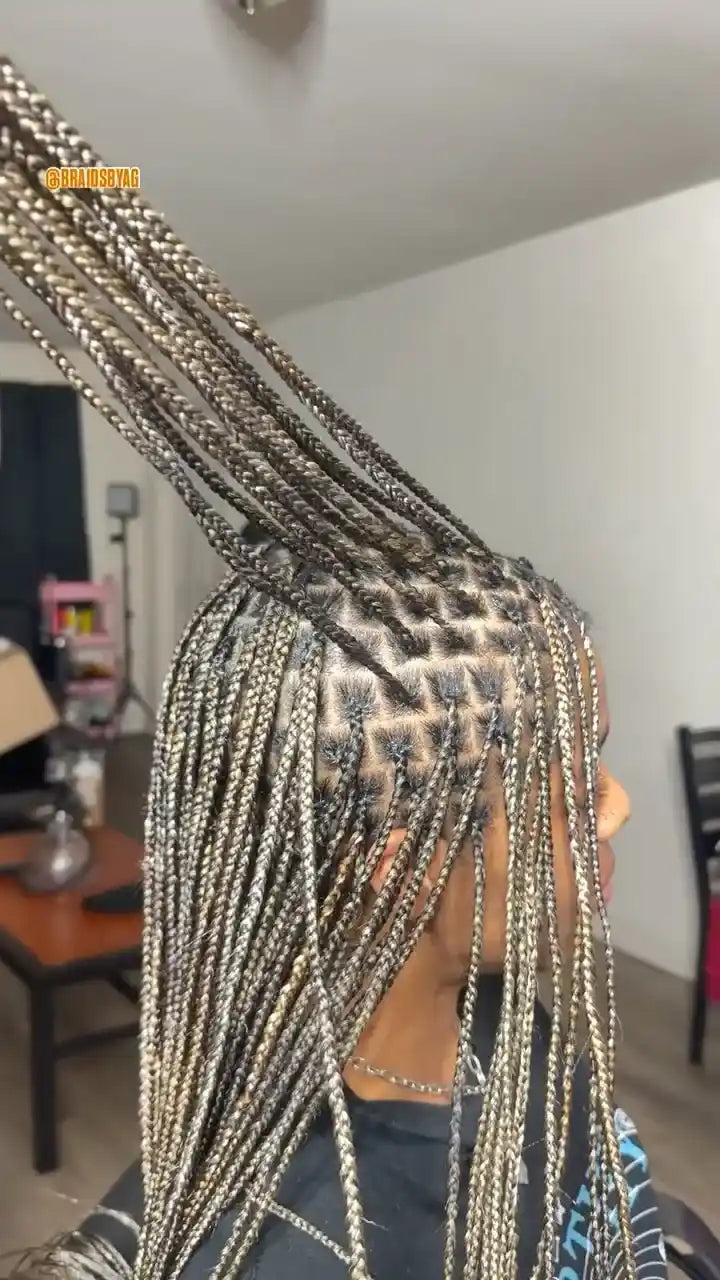 Person with braided hair in a room with a table and chair.