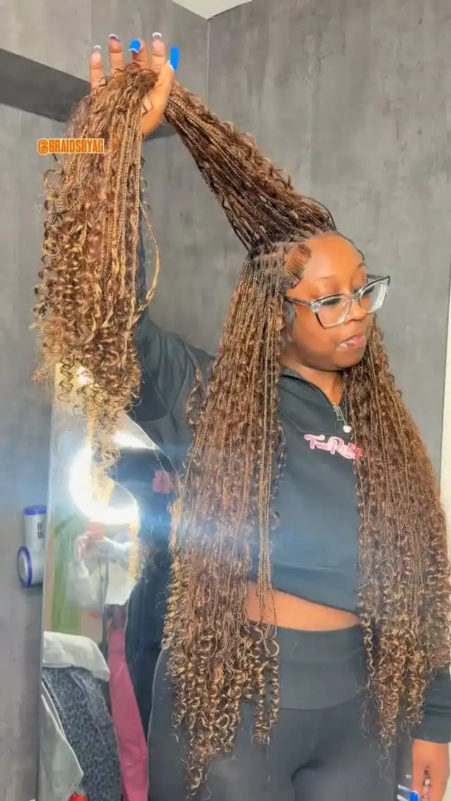 Woman with long braided hair holding a section above her head in a bathroom setting.