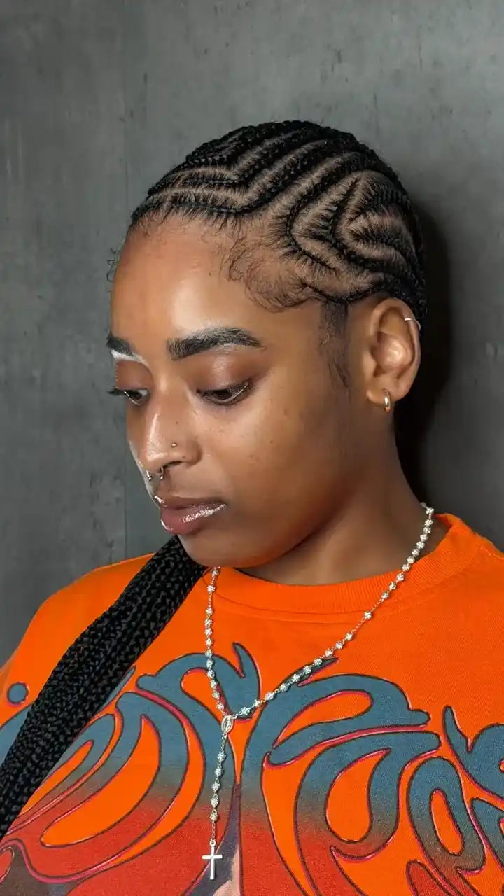 Person with braided hair wearing an orange shirt with a graphic design.