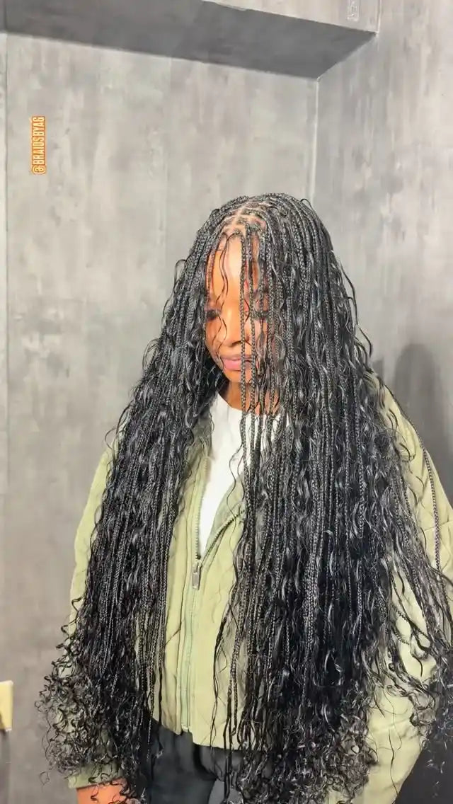 Person with long braided hair standing against a plain wall.