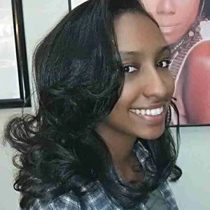 Woman with long, wavy black hair wearing a gray scarf indoors.