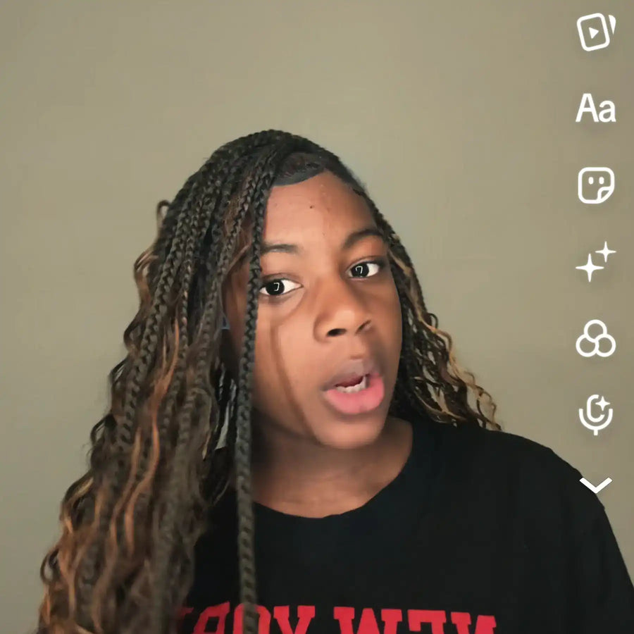 Person with braided hair wearing a black shirt with red text against a plain background