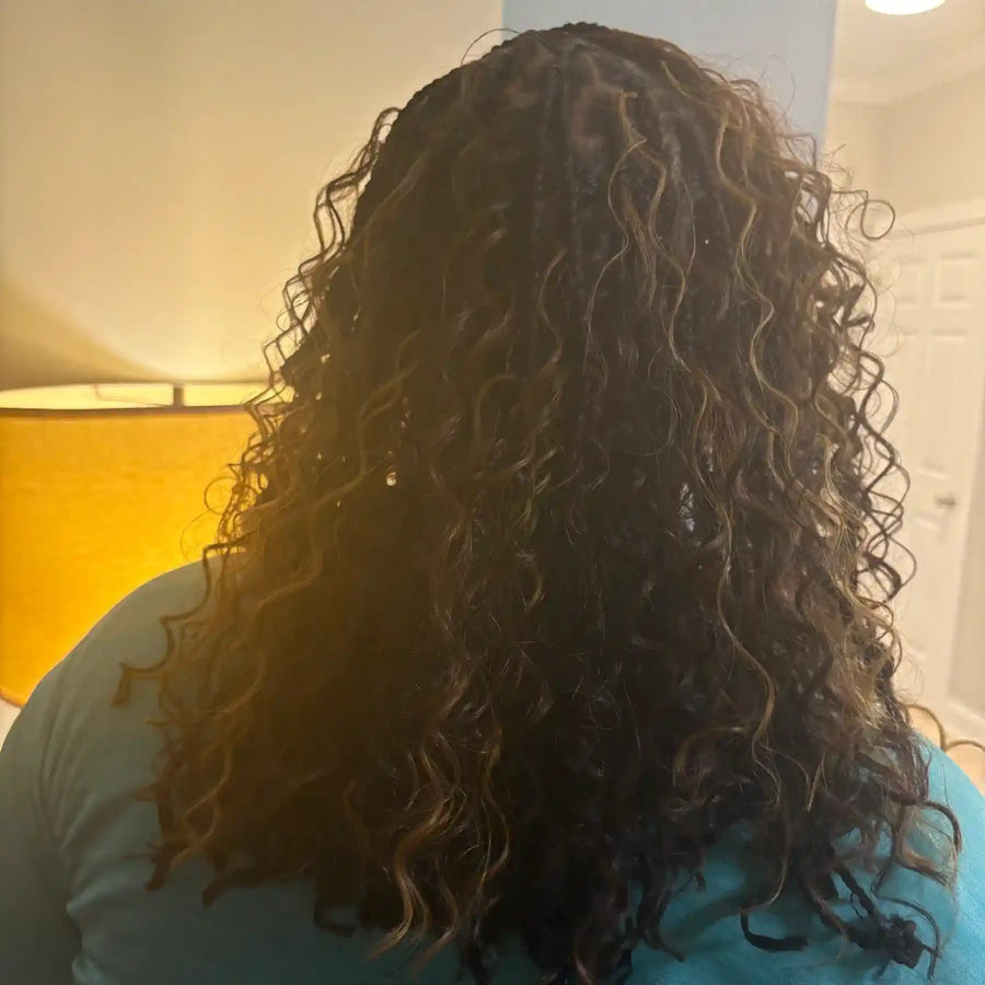 Person with curly hair wearing a blue shirt in a room with a lamp.