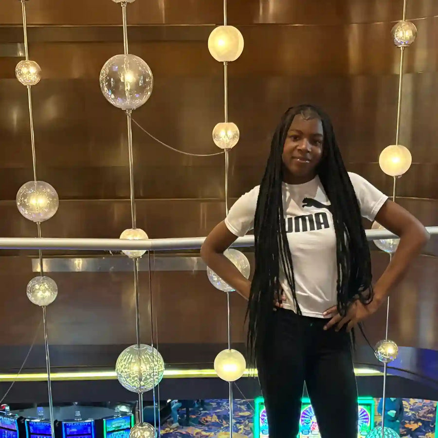 Person wearing a white t-shirt with 'IMA' logo in an indoor setting with hanging lights.