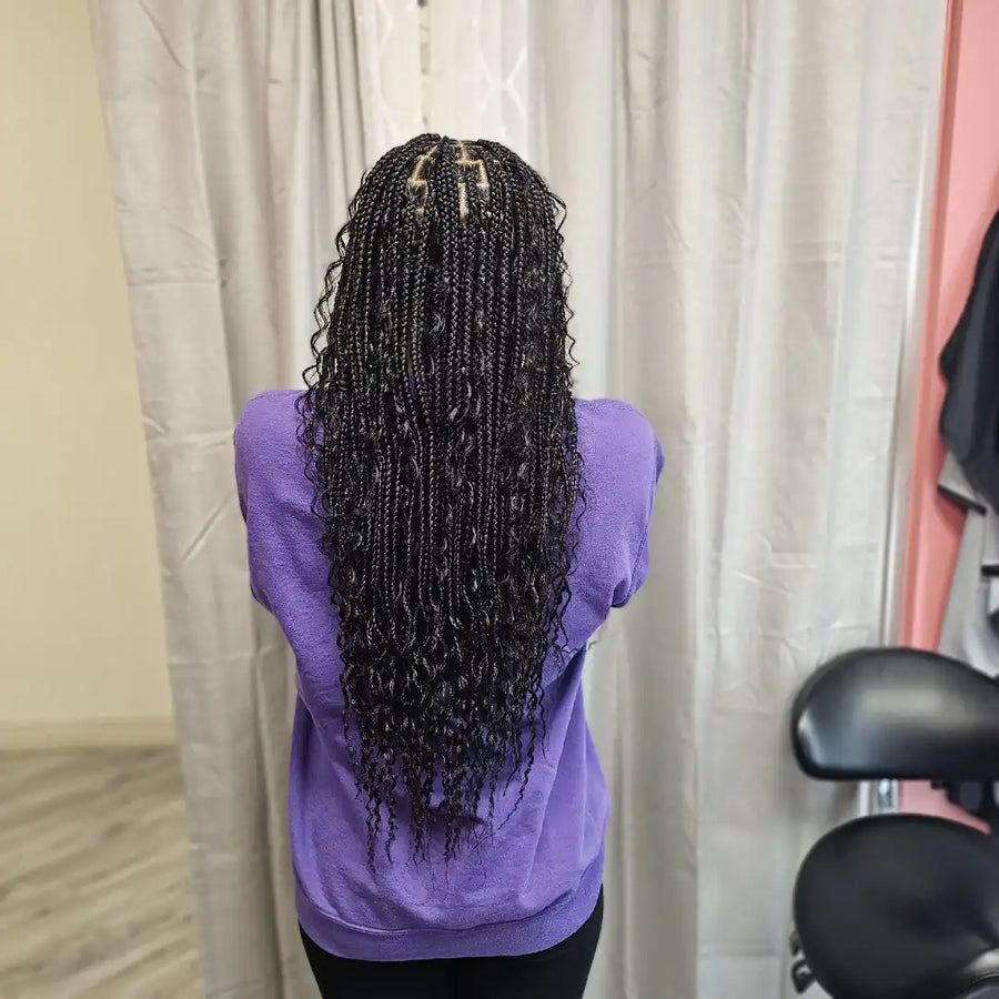 Person with long braided hair wearing a purple shirt in front of a curtain.