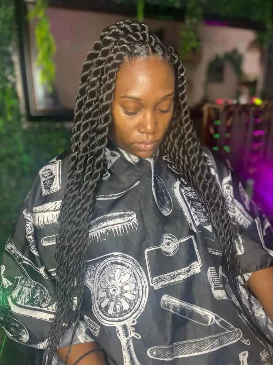 Woman with braided hair wearing a black salon cape with white patterns.