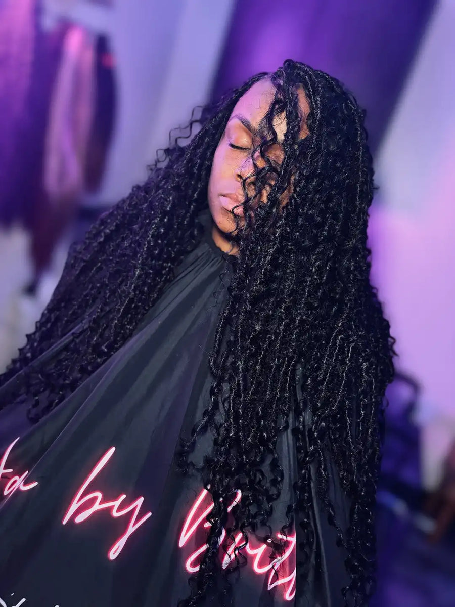 Person with braided hair wearing a black garment with neon text in a blurred indoor setting