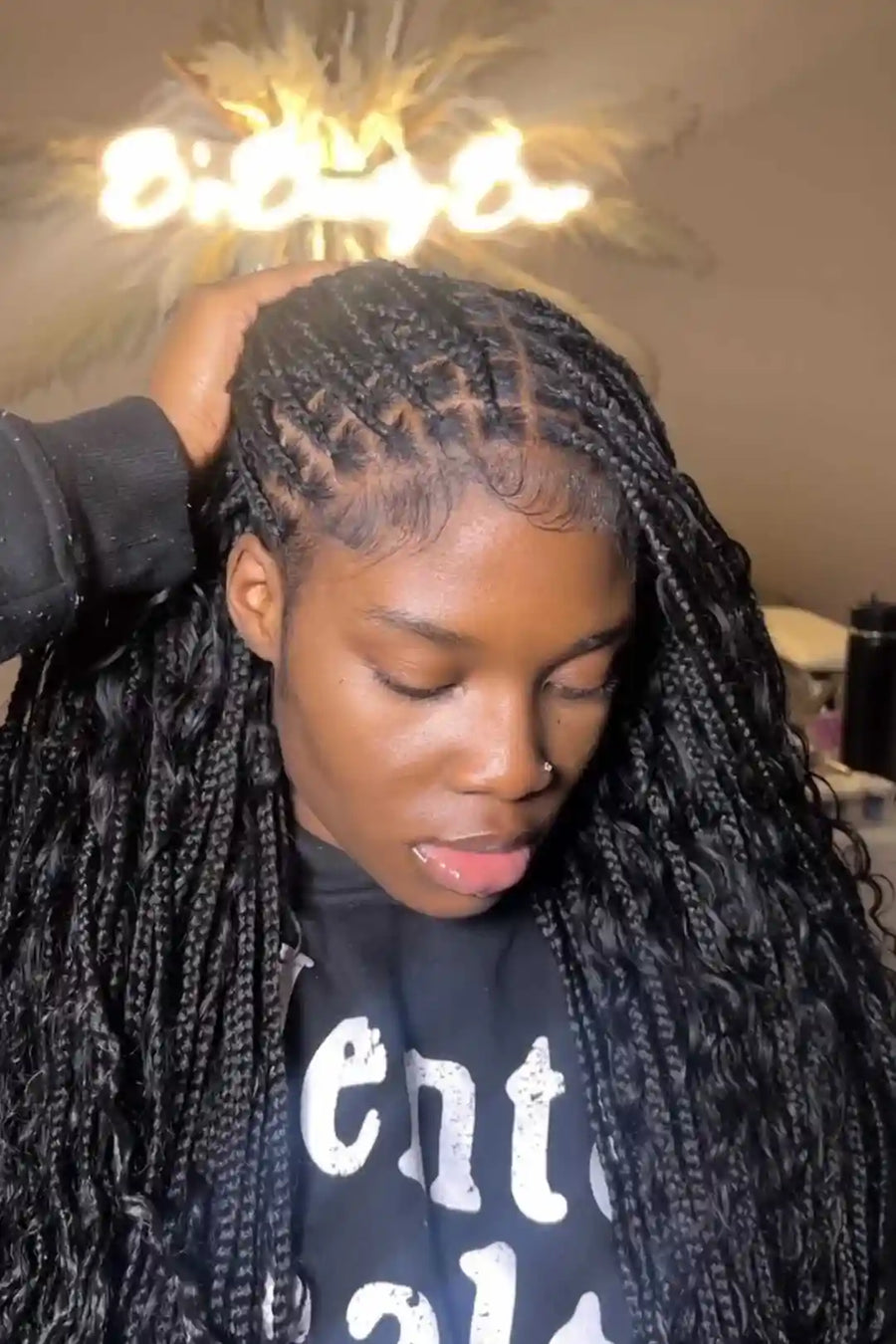 Person with braided hair wearing a black shirt with white text, indoors.