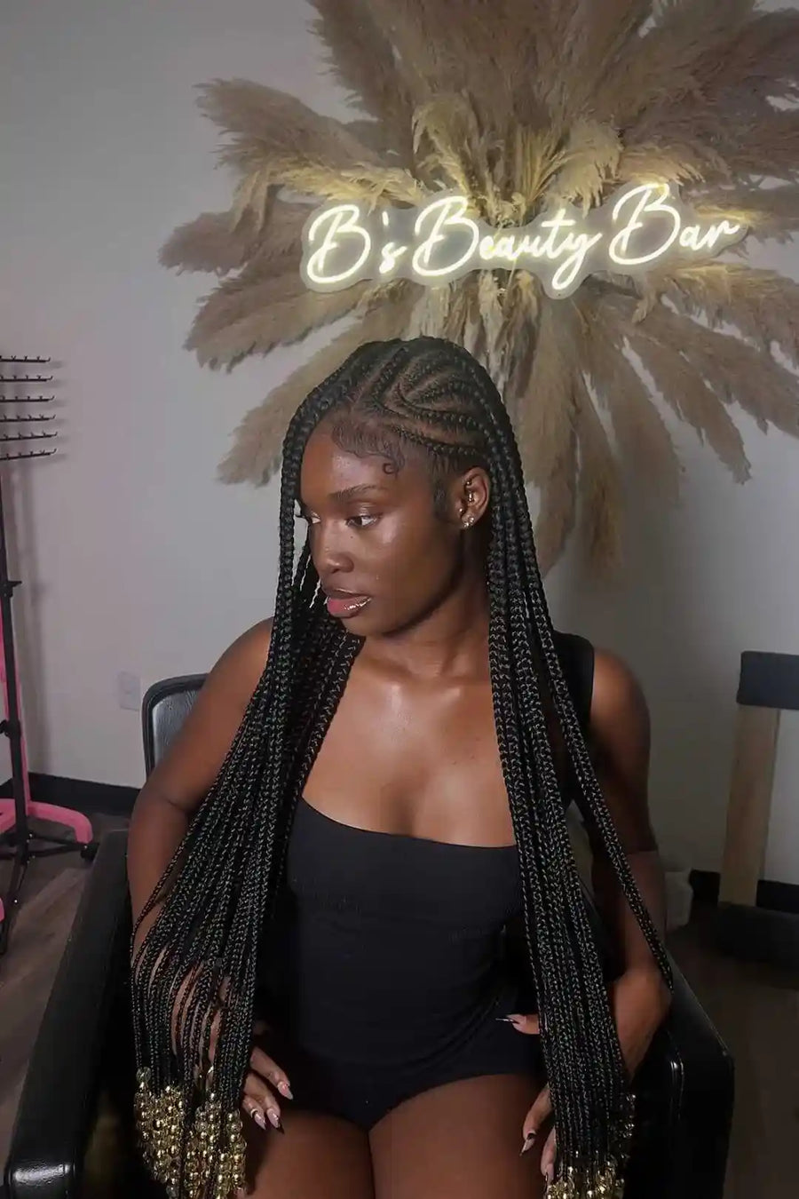 Woman with braided hair in a salon setting with 'B's Beauty Bar' branding.