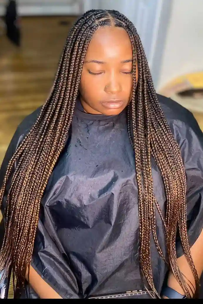Person with long braided hair wearing a black salon cape.