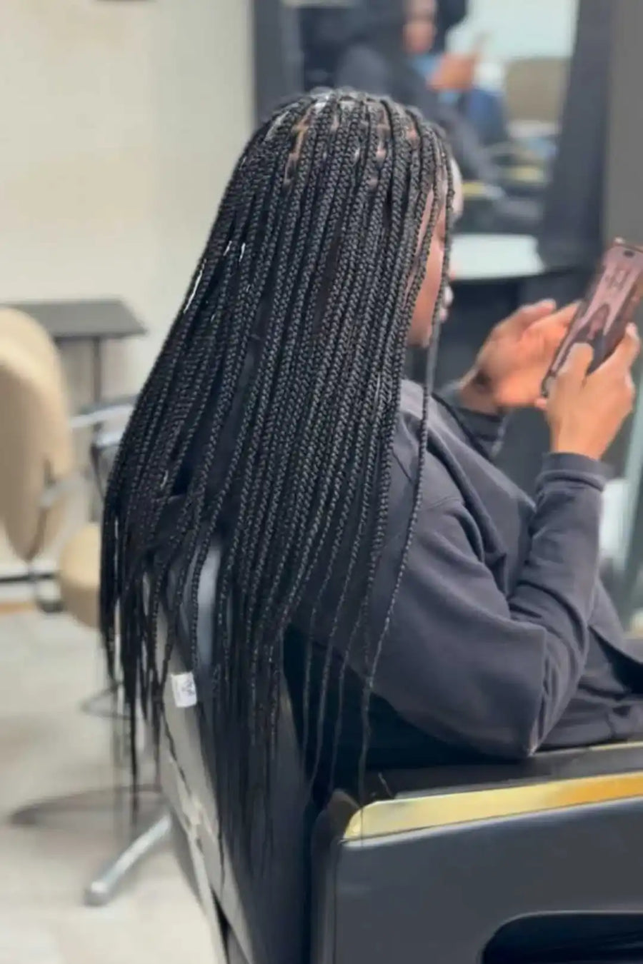 Person with braided hair sitting in a salon chair, using a phone.