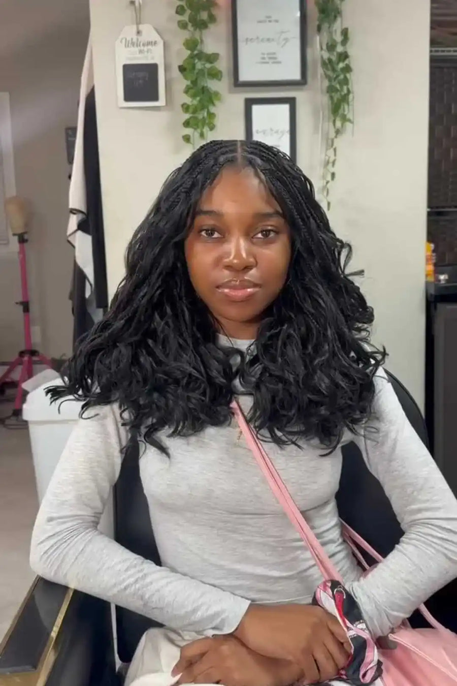 Person with styled hair sitting in a salon chair, holding a pink bag.