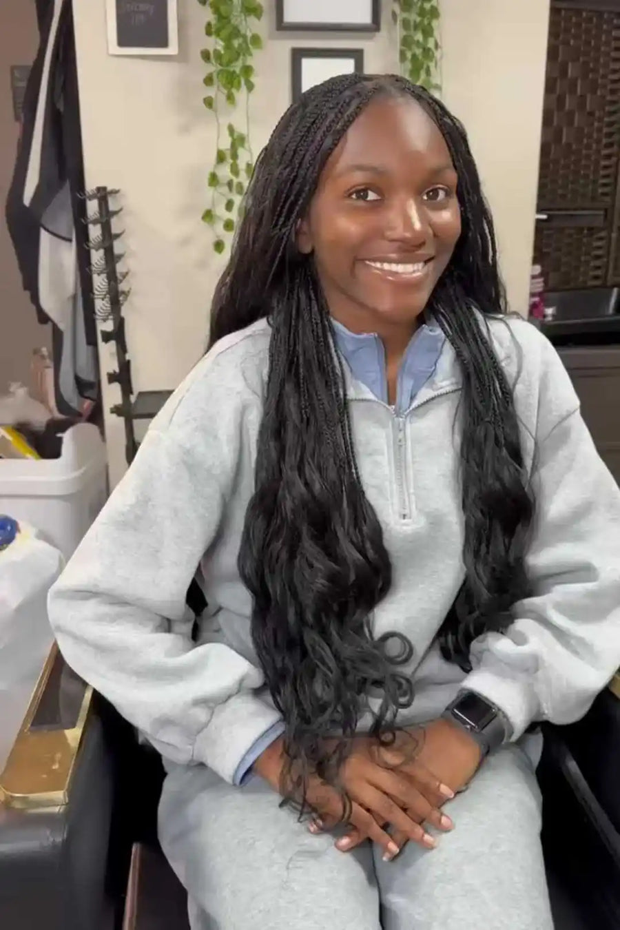Person with long braided hair wearing a gray sweatshirt in a salon setting.
