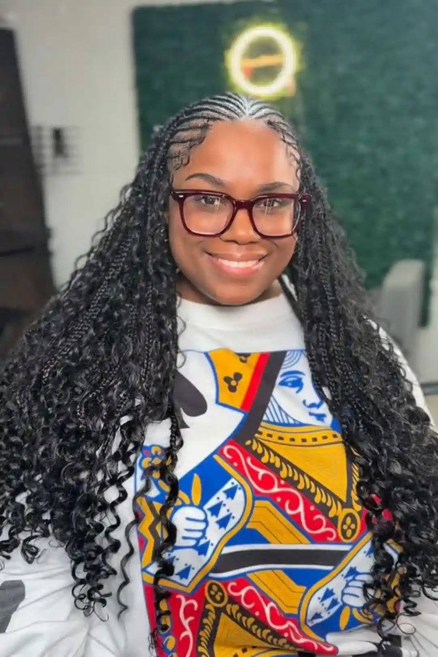 Person with braided hair wearing a colorful shirt with a graphic design.