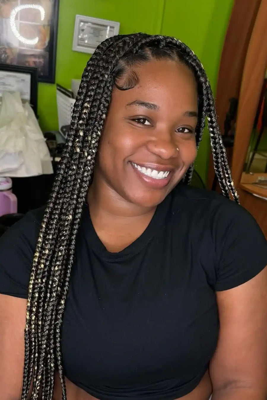 Woman with braided hair smiling in front of a green wall.