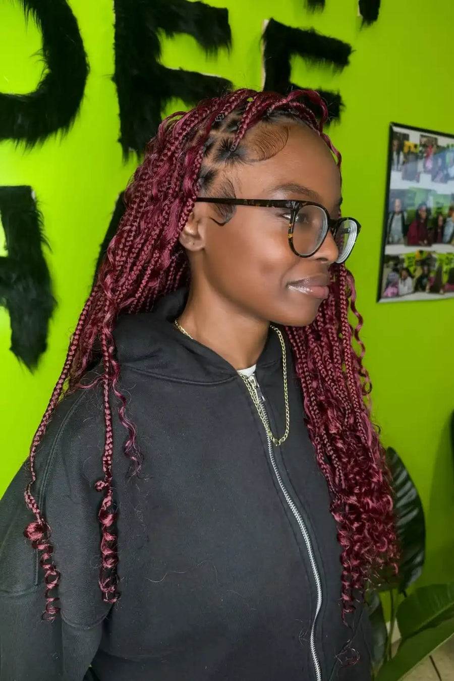 Person with braided hair wearing glasses in front of a bright green wall with text.