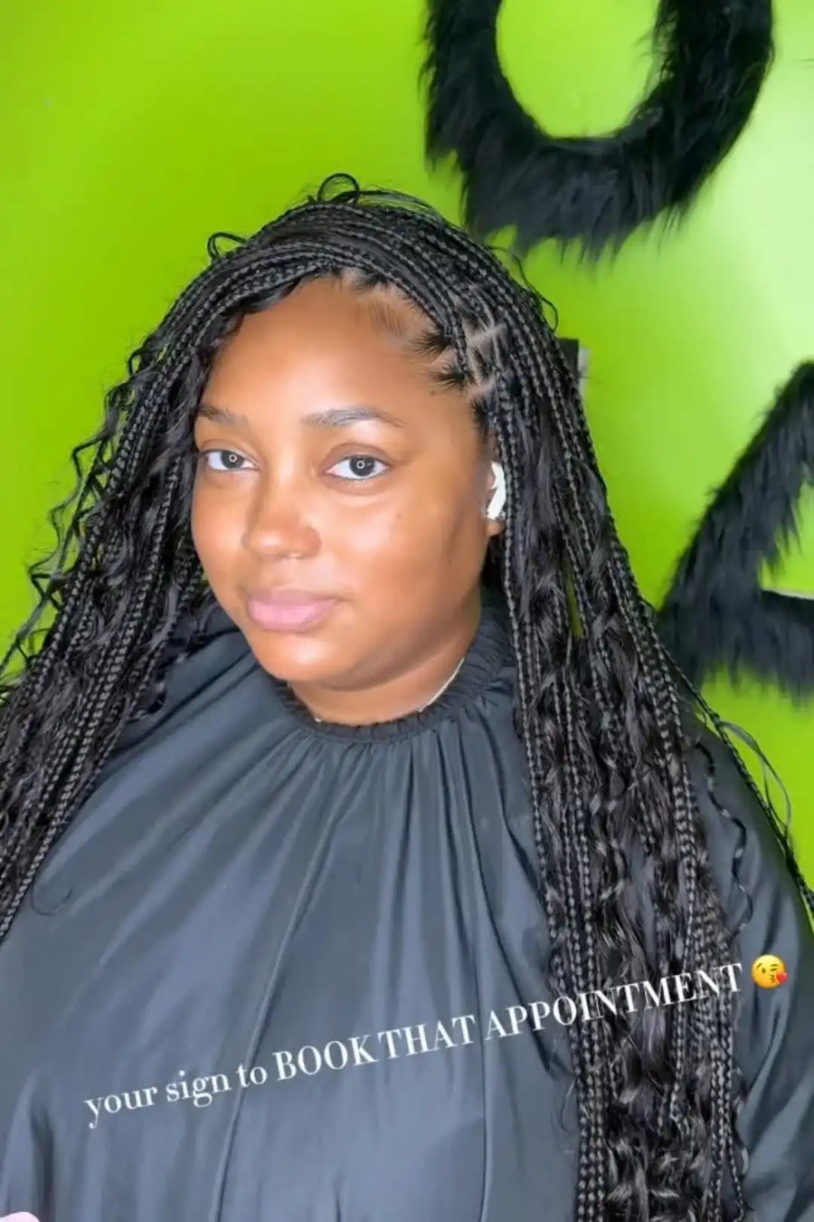 Person with braided hair wearing a black salon cape against a green background