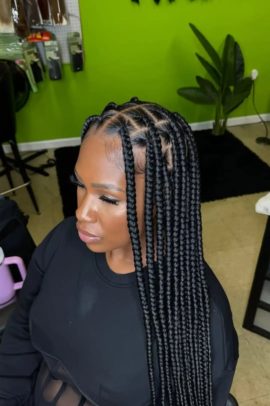Woman with braided hair in a salon setting with green walls and a plant.