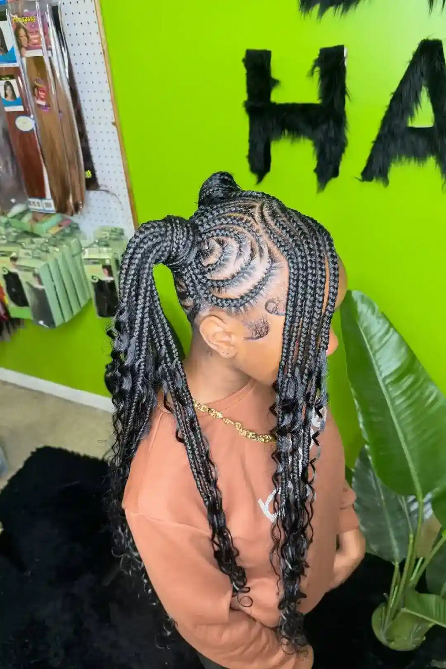 Mannequin head with braided hair against a green wall with 'HA' text