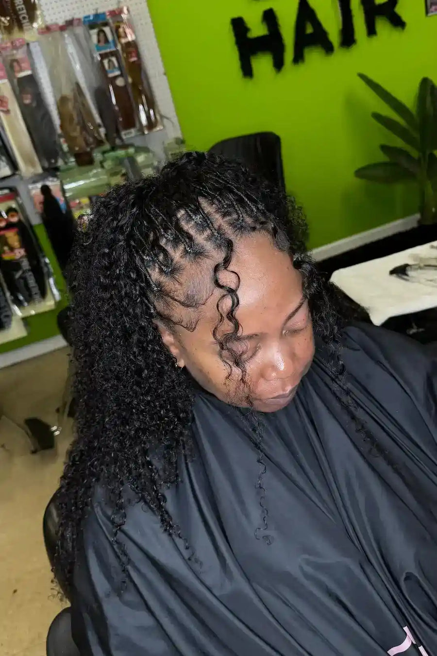 Person with styled hair in a salon setting with a green wall and 'HAIR' sign.