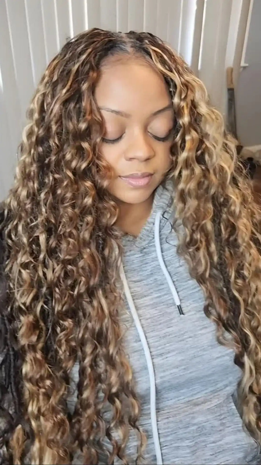 Woman with long, curly hair wearing a gray hoodie indoors.
