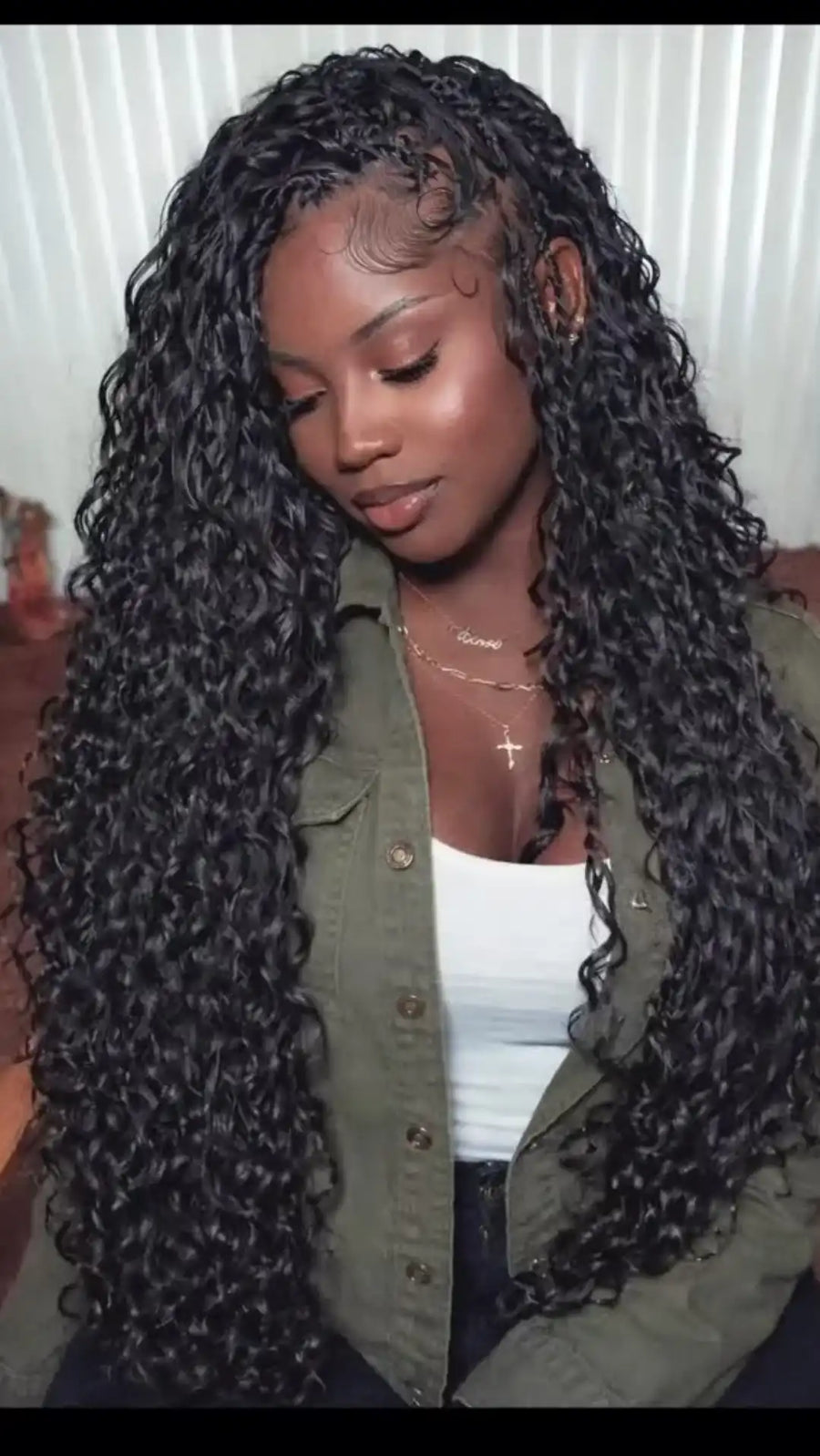 Woman with long, curly hair wearing a green jacket indoors.