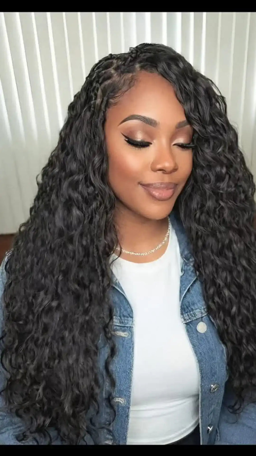 Woman with long, wavy hair wearing a denim jacket indoors.