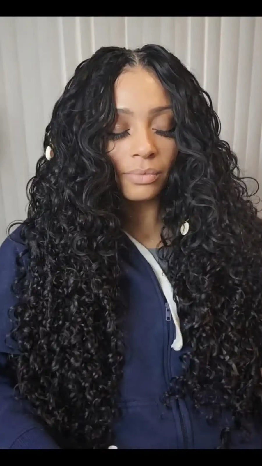 Woman with long, wavy hair wearing a blue jacket against a neutral background