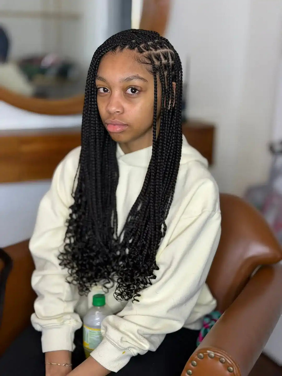 Person with braided hair sitting on a chair, wearing a white hoodie.