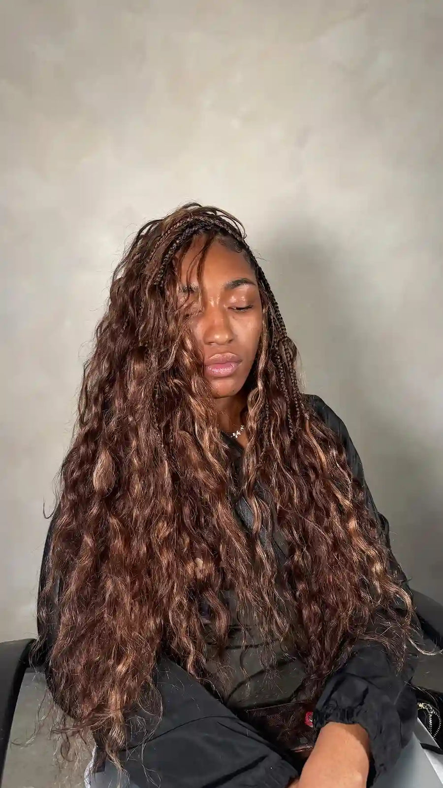 Person with long braided hair sitting against a plain background