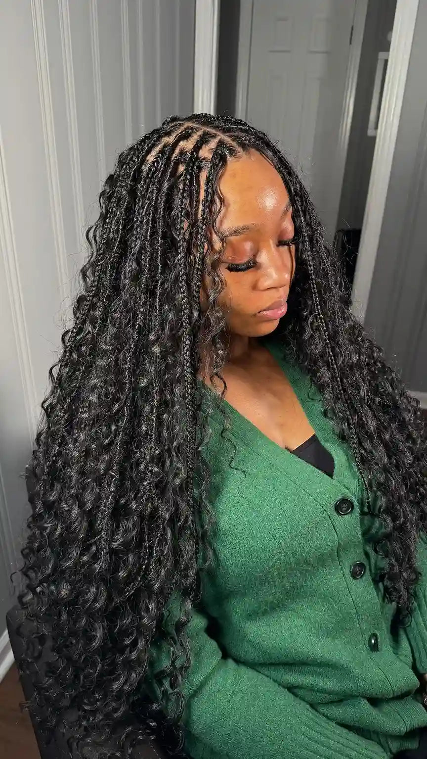 Woman with long braided hair wearing a green sweater indoors.