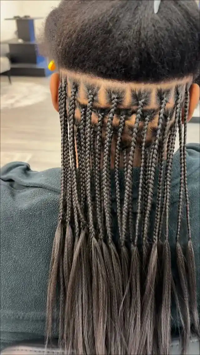 Person with braided hair wearing a black beanie indoors.