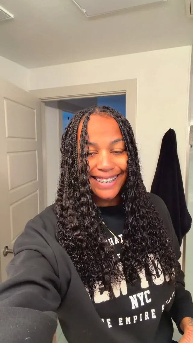 Person with braided hair wearing a black hoodie with white text indoors.