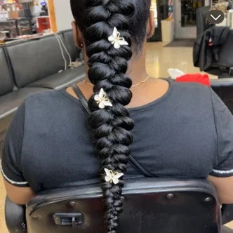 Person with braided hair adorned with flowers in a salon setting