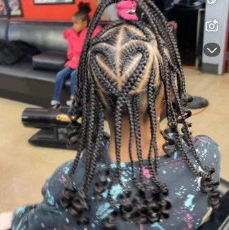 Person with braided hair sitting in a salon chair, with another person in the background.